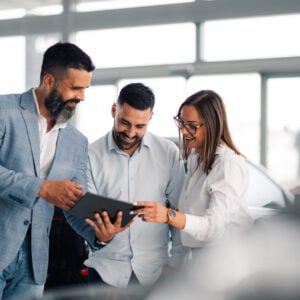 In a sleek car showroom, a professional dealer offers advice and insight to an intrigued couple, enhancing customer satisfaction and decision-making with expert knowledge.