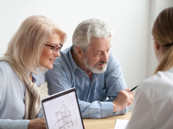 Older couple reading contract at meeting with real estate agent considering new home purchase, realtor or bank worker consulting senior family about buying house loan with project plan on laptop