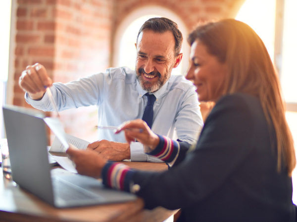 Two middle age business workers smiling happy and confident. Working together with smile on face using laptop at the office