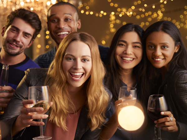 Group of smiling friends posing for picture and holding drinks at a party